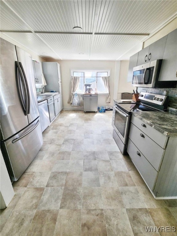 kitchen featuring dark stone countertops, stainless steel appliances, sink, and gray cabinetry