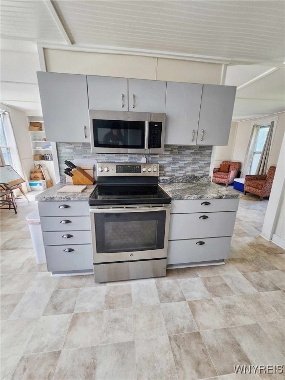 kitchen featuring gray cabinetry, appliances with stainless steel finishes, dark stone counters, and decorative backsplash