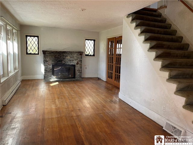 unfurnished living room featuring wood-type flooring, a stone fireplace, a textured ceiling, french doors, and a baseboard radiator