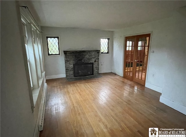 unfurnished living room featuring wood-type flooring, a baseboard heating unit, french doors, and a fireplace