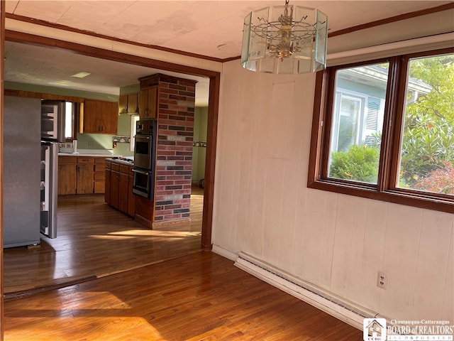 unfurnished dining area featuring baseboard heating, dark hardwood / wood-style flooring, ornamental molding, and an inviting chandelier