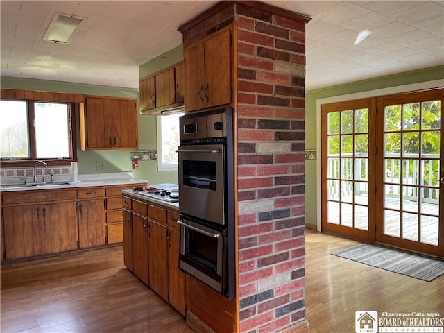 kitchen with double oven, white gas stovetop, sink, and light hardwood / wood-style flooring