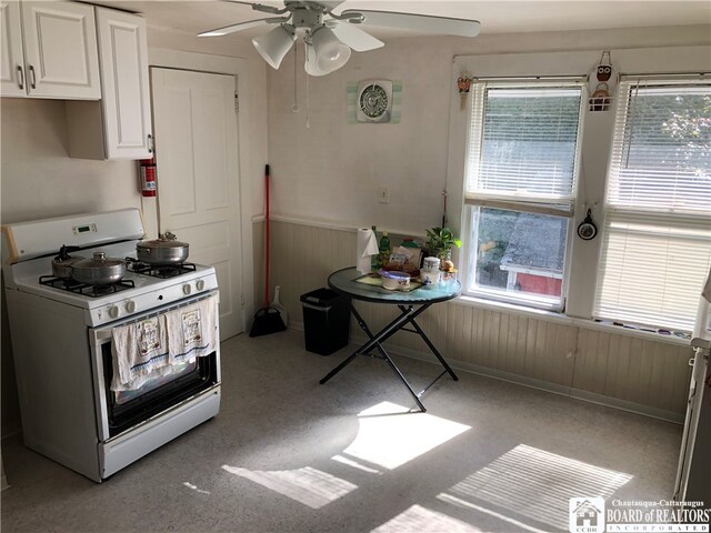 kitchen featuring wooden walls, white range with gas cooktop, white cabinets, and ceiling fan