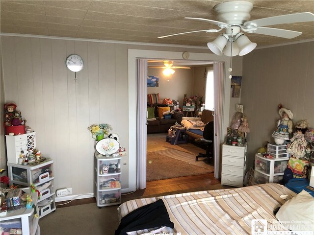 bedroom with ceiling fan, crown molding, dark hardwood / wood-style floors, and wood walls