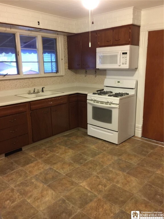 kitchen with ornamental molding, dark brown cabinetry, sink, and white appliances