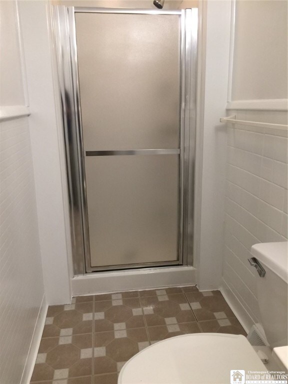 bathroom featuring tile patterned flooring, toilet, and walk in shower