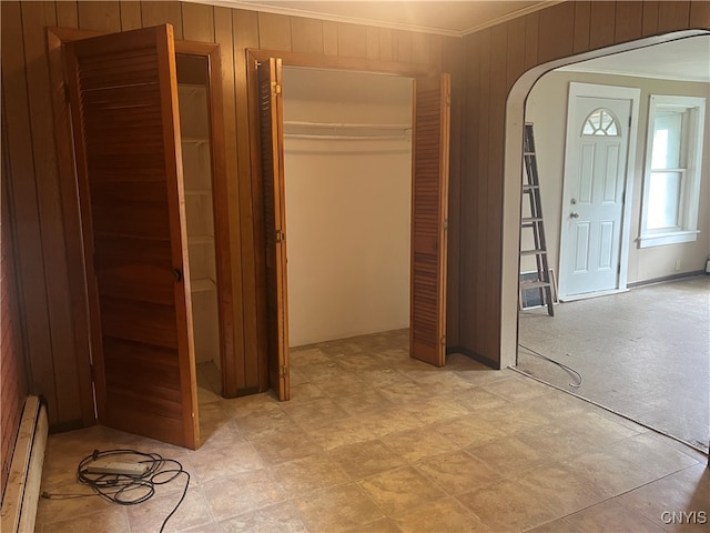 unfurnished bedroom featuring crown molding, baseboard heating, and wooden walls