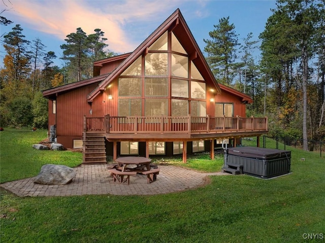 back house at dusk featuring a yard, a patio, a wooden deck, and a hot tub