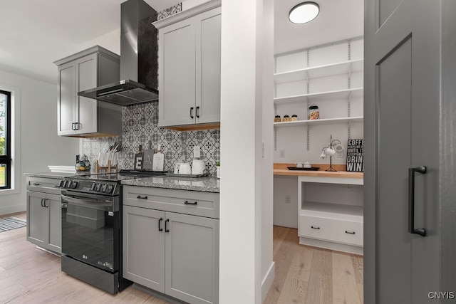 kitchen featuring wall chimney exhaust hood, backsplash, black / electric stove, gray cabinets, and light hardwood / wood-style floors