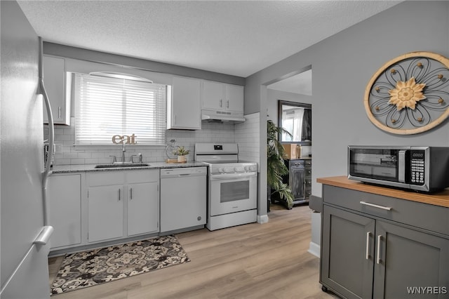 kitchen with light hardwood / wood-style floors, gray cabinets, white appliances, sink, and decorative backsplash