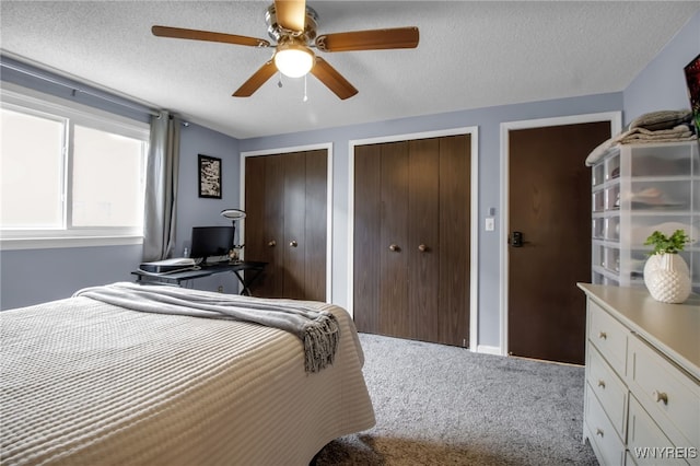 carpeted bedroom with ceiling fan, a textured ceiling, and two closets