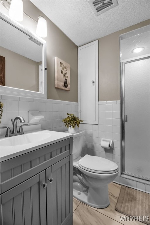 bathroom with tile patterned flooring, walk in shower, toilet, vanity, and a textured ceiling