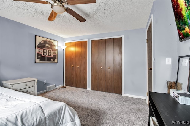 bedroom featuring ceiling fan, a textured ceiling, two closets, and carpet