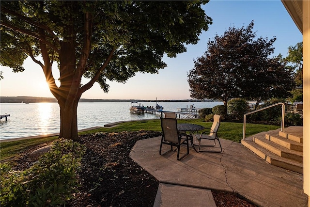 patio terrace at dusk featuring a dock and a water view