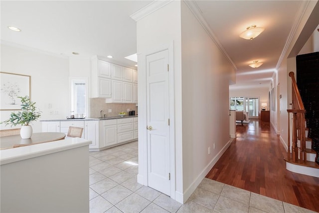 corridor with light tile patterned flooring, a sink, baseboards, and ornamental molding