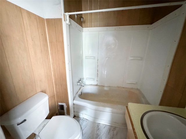 full bathroom with vanity, wooden walls, bathtub / shower combination, and toilet