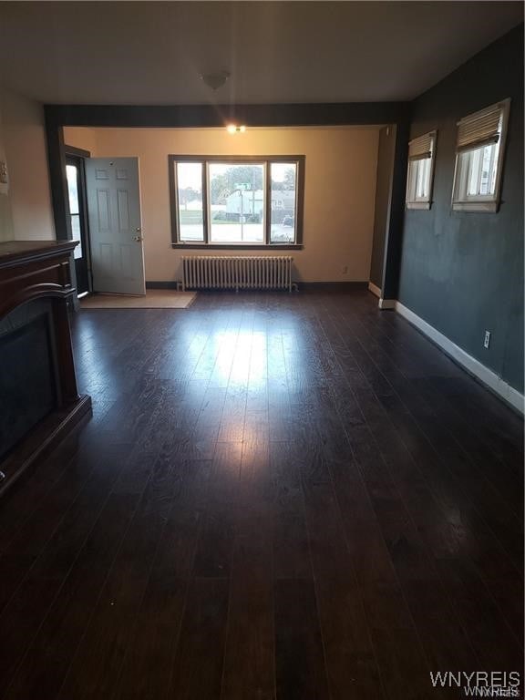 unfurnished living room with dark wood-type flooring and radiator heating unit