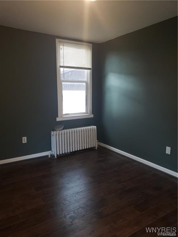 unfurnished room featuring radiator heating unit and dark hardwood / wood-style flooring