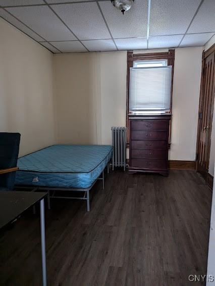 bedroom with a paneled ceiling, radiator heating unit, and dark wood-style floors