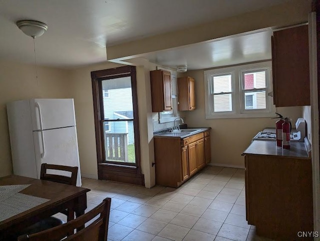 kitchen featuring a healthy amount of sunlight, light tile patterned floors, freestanding refrigerator, and a sink