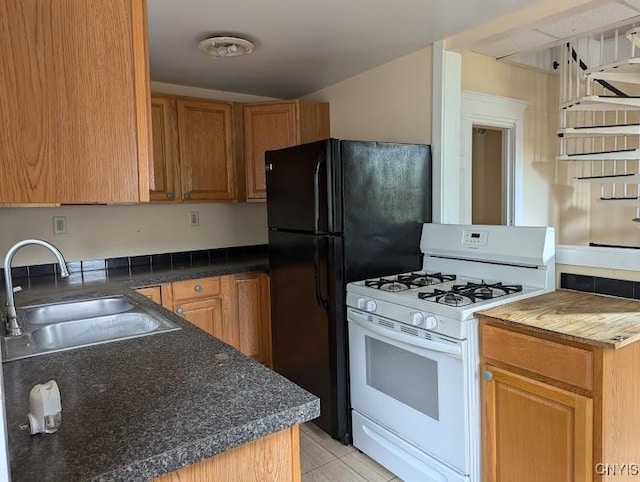 kitchen featuring light tile patterned flooring, dark countertops, a sink, freestanding refrigerator, and white range with gas stovetop
