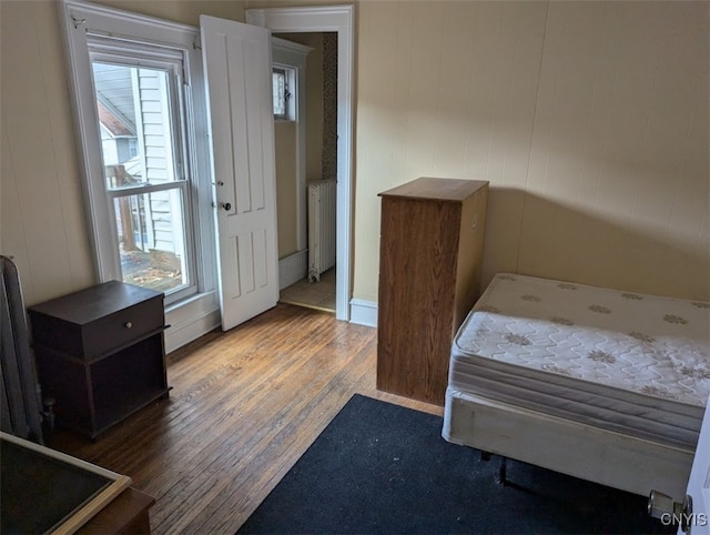 bedroom with dark hardwood / wood-style floors, radiator heating unit, and wooden walls