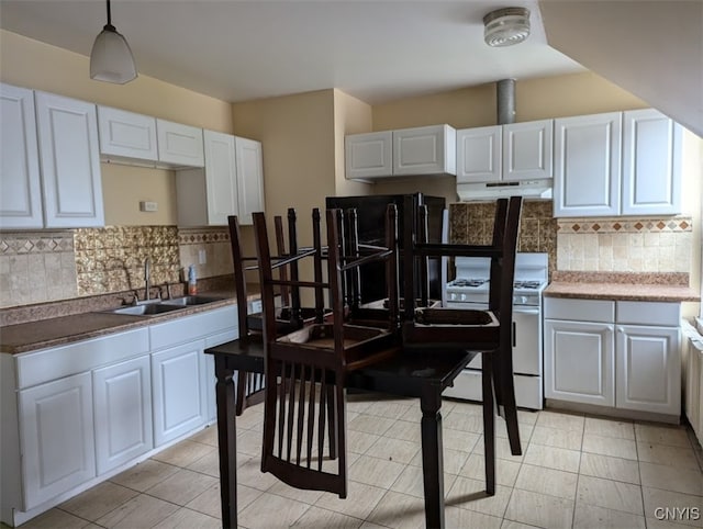 kitchen with white stove, sink, hanging light fixtures, white cabinetry, and backsplash