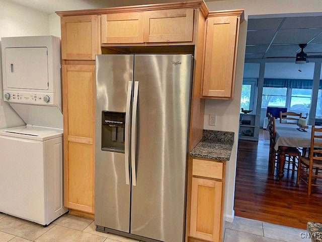 kitchen with light brown cabinetry, light hardwood / wood-style floors, stacked washer and dryer, dark stone countertops, and stainless steel refrigerator with ice dispenser