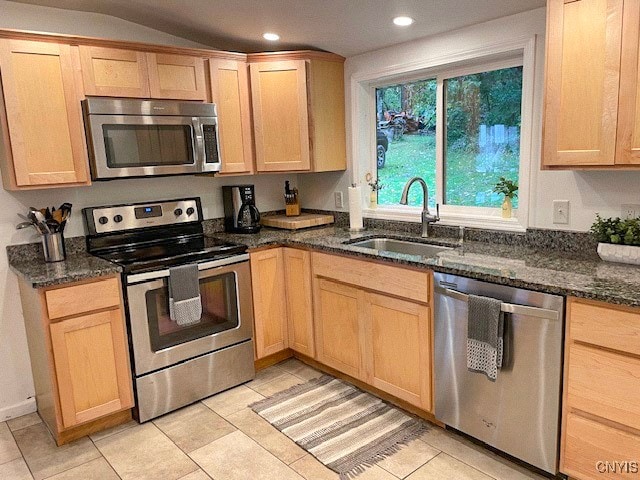 kitchen with light tile patterned floors, appliances with stainless steel finishes, light brown cabinetry, dark stone countertops, and sink