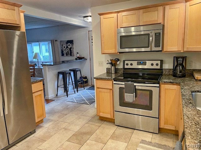 kitchen with light brown cabinets, stainless steel appliances, and dark stone counters