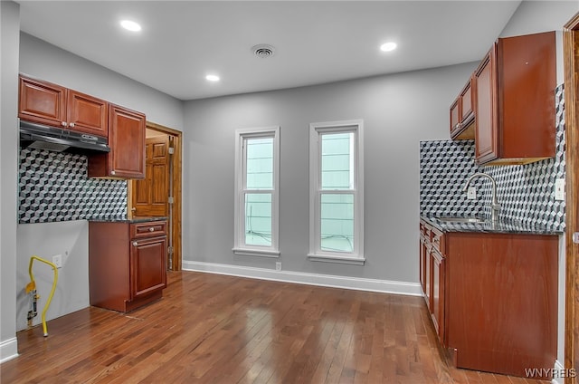 kitchen featuring dark stone counters, sink, wood-type flooring, and backsplash