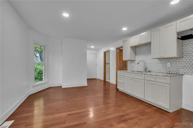 kitchen with tasteful backsplash, dark hardwood / wood-style flooring, light stone counters, sink, and white cabinets