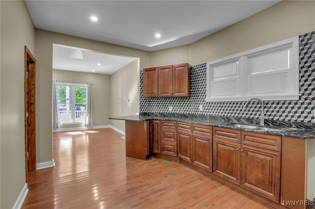 kitchen featuring backsplash, dark stone countertops, light hardwood / wood-style flooring, and sink