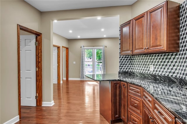 kitchen featuring kitchen peninsula, dark stone counters, wood-type flooring, and tasteful backsplash