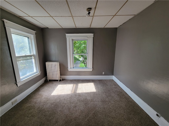 carpeted spare room featuring a paneled ceiling, a healthy amount of sunlight, and radiator heating unit