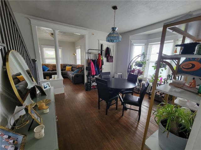 dining area with ornate columns, a healthy amount of sunlight, a textured ceiling, and dark hardwood / wood-style floors