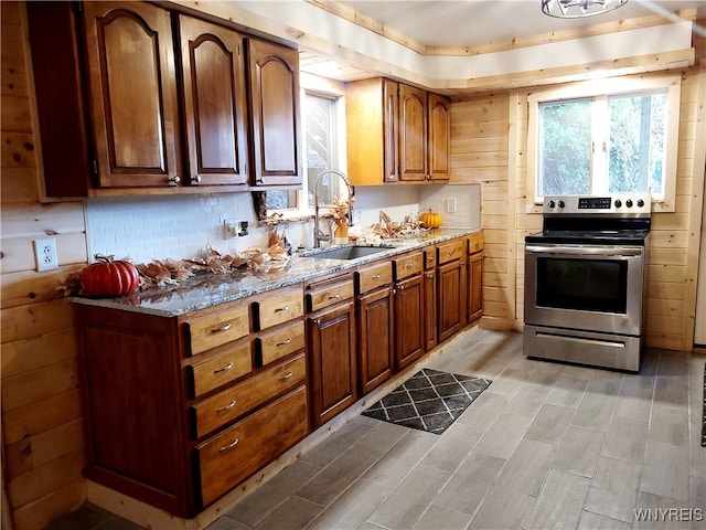 kitchen featuring wood walls, sink, light wood-type flooring, electric range, and light stone counters