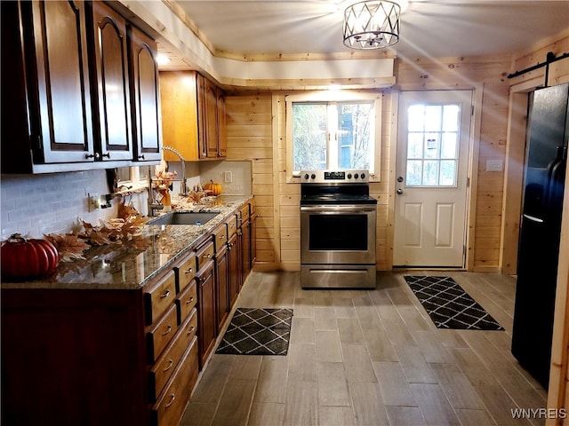 kitchen featuring wood walls, a barn door, stainless steel range with electric cooktop, and sink