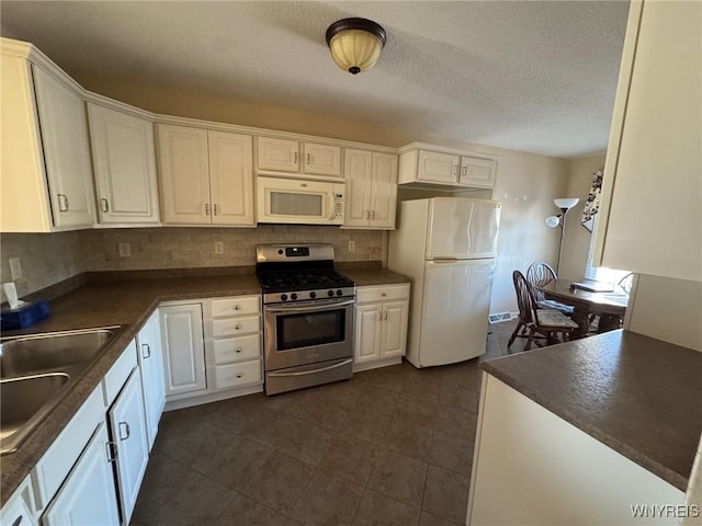 kitchen featuring white appliances, dark countertops, a sink, and white cabinetry