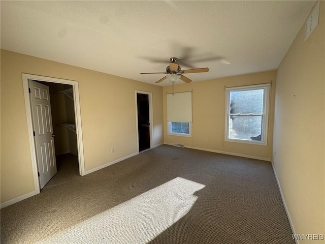 unfurnished bedroom featuring baseboards, visible vents, ceiling fan, carpet, and a walk in closet