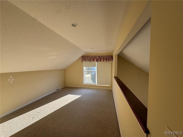 additional living space featuring a textured ceiling, lofted ceiling, carpet flooring, visible vents, and baseboards