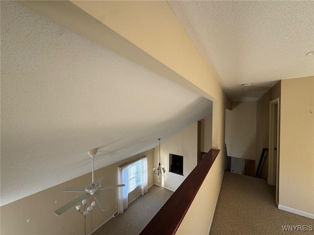 hall with lofted ceiling, a textured ceiling, carpet flooring, and an upstairs landing