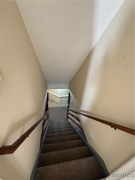 stairs featuring a textured ceiling and carpet flooring