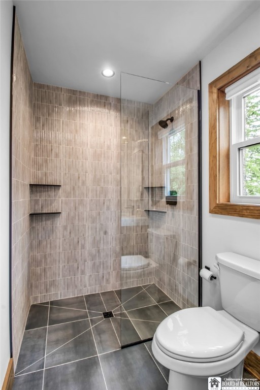 bathroom with a tile shower, toilet, and tile patterned flooring