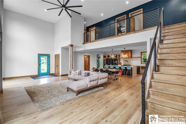 living room featuring a high ceiling, ceiling fan, light hardwood / wood-style floors, and decorative columns