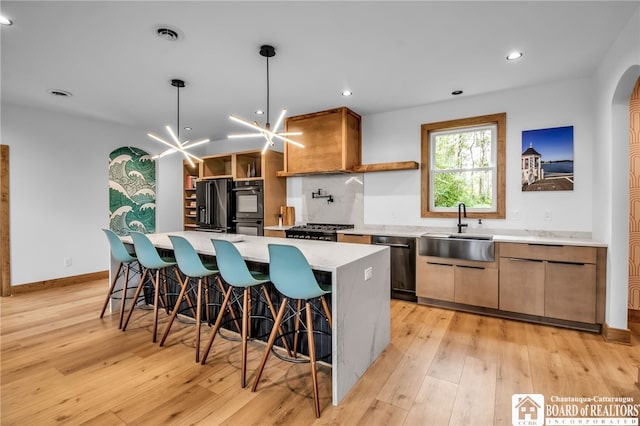 kitchen featuring a kitchen island, light hardwood / wood-style flooring, sink, black appliances, and a notable chandelier