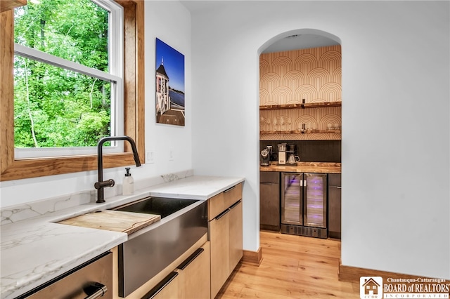 bar featuring a healthy amount of sunlight, light stone counters, light wood-type flooring, and beverage cooler