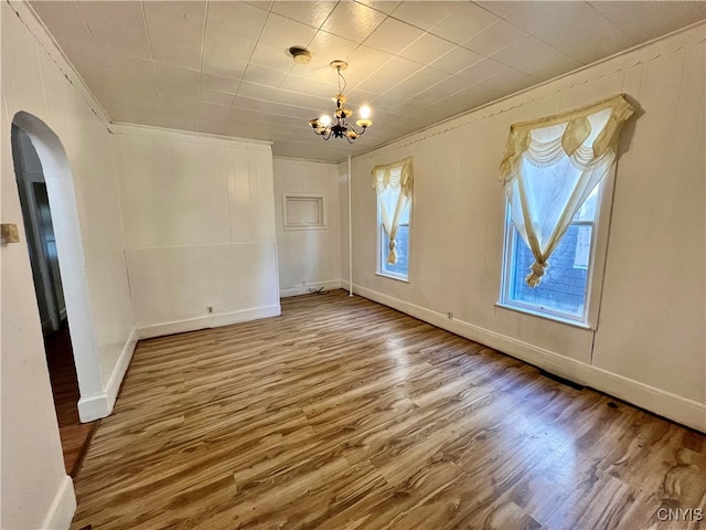 empty room with an inviting chandelier, hardwood / wood-style flooring, and crown molding