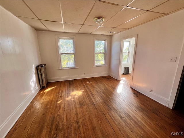 empty room featuring dark wood-type flooring, a paneled ceiling, and radiator heating unit