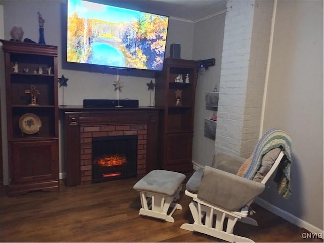 sitting room featuring a brick fireplace, baseboards, ornamental molding, and wood finished floors